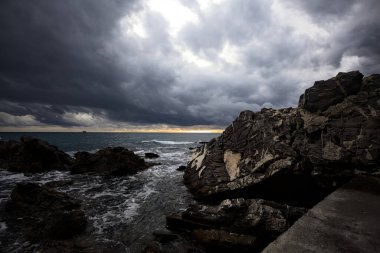 Alacakaranlıkta bulutlu bir günde kayalara vuran suyla dalgalı su