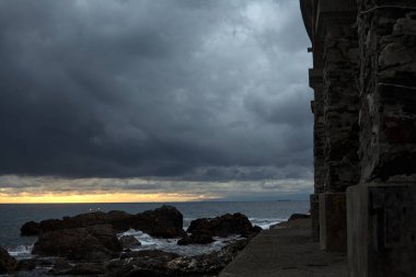 Deniz kıyısındaki bir viyadük kemerleri, bir dalgakıranın kayaları üzerinde, alacakaranlıkta bulutlu bir günde görülür.