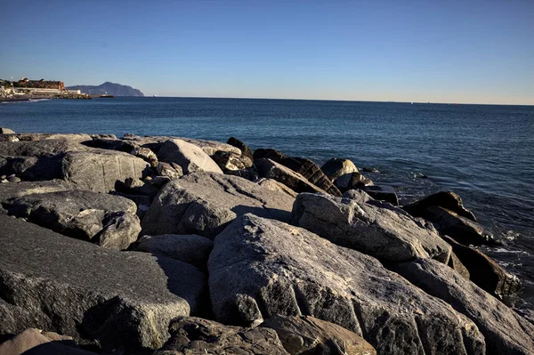 Küçük bir körfezden görünen ve dalgakıran kayaları tarafından çerçevelenen binalar ve uçurumun kenarındaki bir çıkıntının ucu.