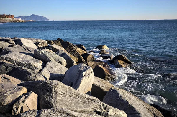 Küçük bir körfezden görünen ve dalgakıran kayaları tarafından çerçevelenen binalar ve uçurumun kenarındaki bir çıkıntının ucu.