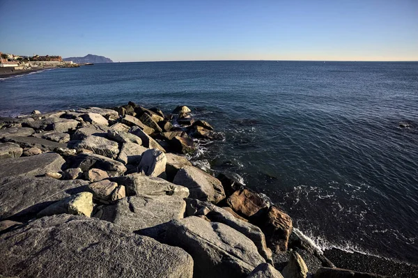 Küçük bir körfezden görünen ve dalgakıran kayaları tarafından çerçevelenen binalar ve uçurumun kenarındaki bir çıkıntının ucu.