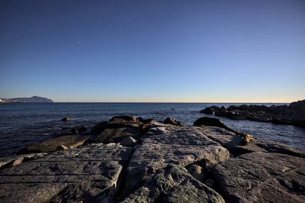 Gün batımında bir uçurumun kayaları su seviyesinde görülür ve deniz Horizon 'a kadar uzanır.
