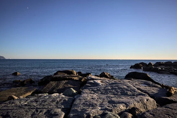 Gün batımında bir uçurumun kayaları su seviyesinde görülür ve deniz Horizon 'a kadar uzanır.