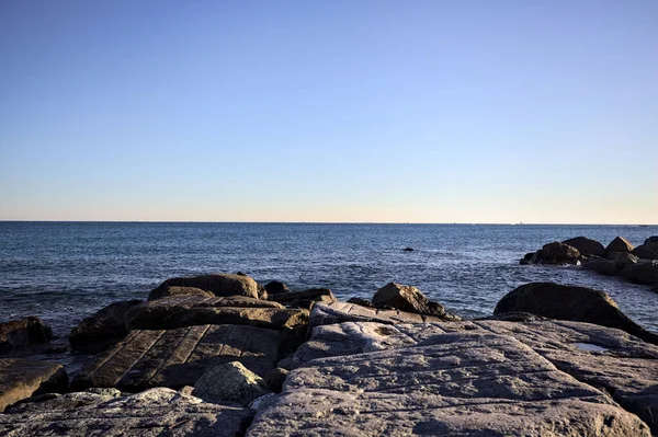 Gün batımında bir uçurumun kayaları su seviyesinde görülür ve deniz Horizon 'a kadar uzanır.