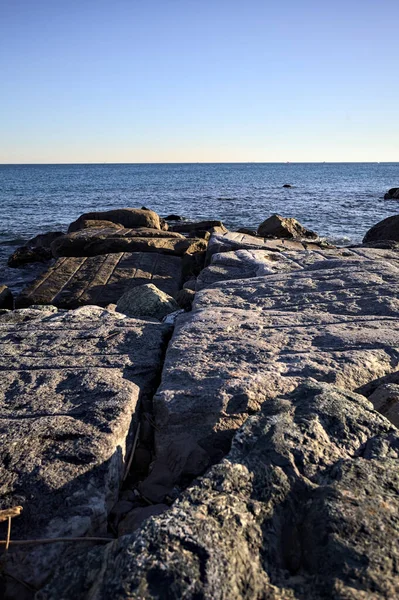Rocks of a cliff at sunset seen at water level with the sea stretching to the Horizon
