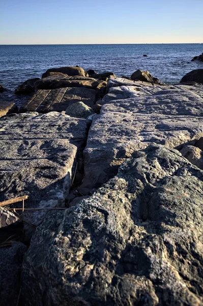 Rocks of a cliff at sunset seen at water level with the sea stretching to the Horizon