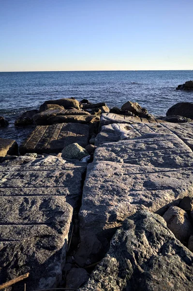 Rocks of a cliff at sunset seen at water level with the sea stretching to the Horizon