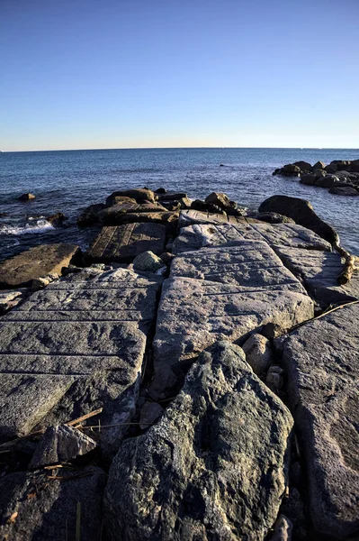 Rocks of a cliff at sunset seen at water level with the sea stretching to the Horizon