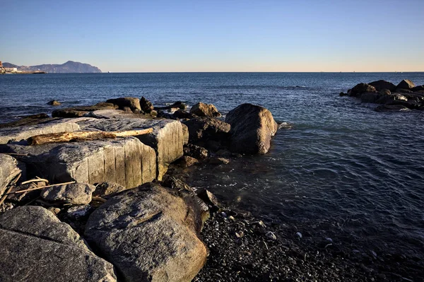 Küçük bir körfezden görünen ve dalgakıran kayaları tarafından çerçevelenen binalar ve uçurumun kenarındaki bir çıkıntının ucu.