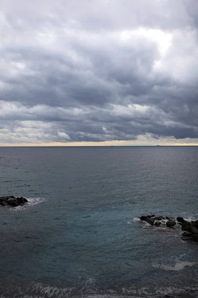 Alacakaranlıkta bulutlu bir günde ufka doğru uzanan deniz yukarıdan görünen küçük bir koydan kayalarla birlikte.
