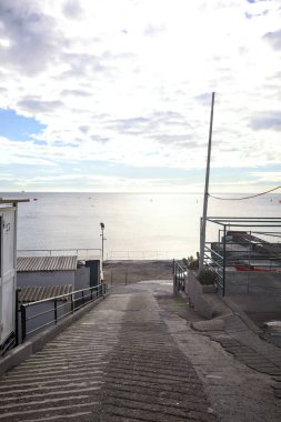 Kışın bulutlu bir günde, deniz ve sahili çerçeveletip ufka kadar uzanan beton bir geçide tırmanmak.