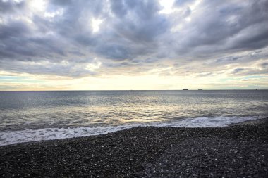 Bir kış günü, gün batımında, sahilde dalgalar eziliyor.