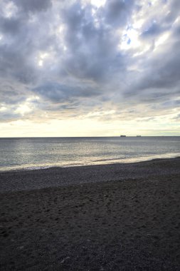 Bir kış günü, gün batımında, sahilde dalgalar eziliyor.