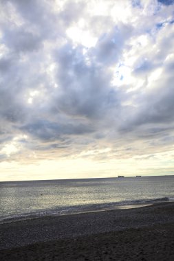 Bir kış günü, gün batımında, sahilde dalgalar eziliyor.