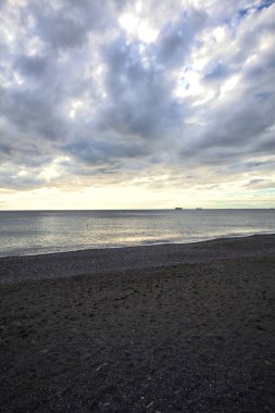 Bir kış günü, gün batımında, sahilde dalgalar eziliyor.