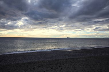 Bir kış günü, gün batımında, sahilde dalgalar eziliyor.