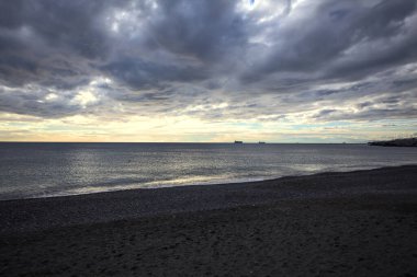 Bir kış günü, gün batımında, sahilde dalgalar eziliyor.