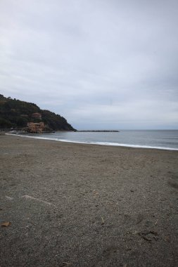 Kışın bulutlu bir günde, kumsalda bir bina, arka planda ağaçlarla kaplı bir uçurum ve uçurumun kenarında bir dalgakıran.