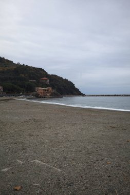 Kışın bulutlu bir günde, kumsalda bir bina, arka planda ağaçlarla kaplı bir uçurum ve uçurumun kenarında bir dalgakıran.
