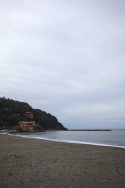 Kışın bulutlu bir günde, kumsalda bir bina, arka planda ağaçlarla kaplı bir uçurum ve uçurumun kenarında bir dalgakıran.