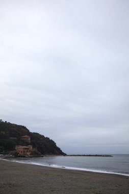 Kışın bulutlu bir günde, kumsalda bir bina, arka planda ağaçlarla kaplı bir uçurum ve uçurumun kenarında bir dalgakıran.