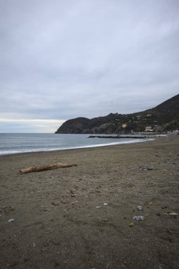 Dalgalar denize doğru uzanıyor, kapalı tatil beldeleri olan bir sahilde ve arka planda bir kasabanın binaları, kışın bulutlu bir günde.