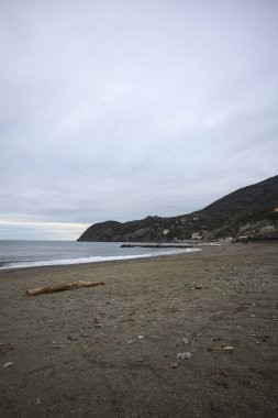 Dalgalar denize doğru uzanıyor, kapalı tatil beldeleri olan bir sahilde ve arka planda bir kasabanın binaları, kışın bulutlu bir günde.
