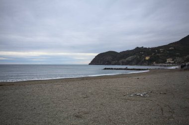 Dalgalar denize doğru uzanıyor, kapalı tatil beldeleri olan bir sahilde ve arka planda bir kasabanın binaları, kışın bulutlu bir günde.