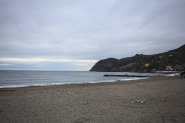 Dalgalar denize doğru uzanıyor, kapalı tatil beldeleri olan bir sahilde ve arka planda bir kasabanın binaları, kışın bulutlu bir günde.