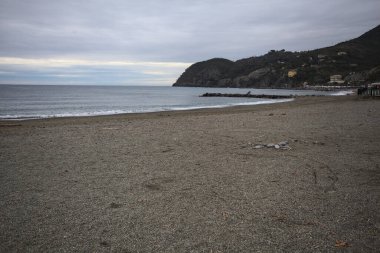Dalgalar denize doğru uzanıyor, kapalı tatil beldeleri olan bir sahilde ve arka planda bir kasabanın binaları, kışın bulutlu bir günde.