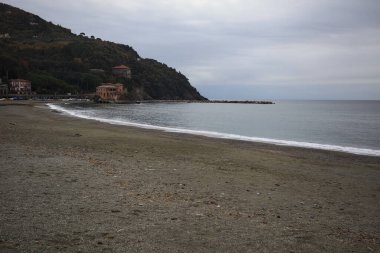 Kışın bulutlu bir günde, kumsalda bir bina, arka planda ağaçlarla kaplı bir uçurum ve uçurumun kenarında bir dalgakıran.