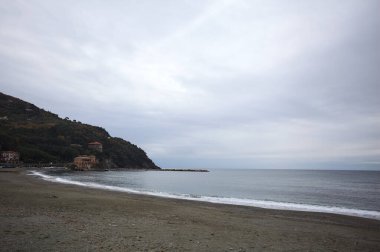 Kışın bulutlu bir günde, kumsalda bir bina, arka planda ağaçlarla kaplı bir uçurum ve uçurumun kenarında bir dalgakıran.