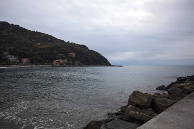 Kışın bulutlu bir günde, kumsalda bir bina, arka planda ağaçlarla kaplı bir uçurum ve uçurumun kenarında bir dalgakıran.