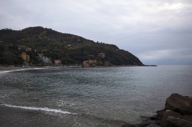 Kışın bulutlu bir günde, kumsalda bir bina, arka planda ağaçlarla kaplı bir uçurum ve uçurumun kenarında bir dalgakıran.