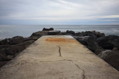 Kışın bulutlu bir günde dalgaların kayalara çarptığı ve denizin ufka doğru genişlediği dalgalı bir platformda.