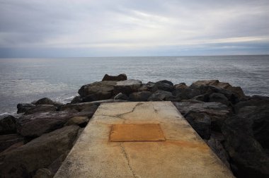 Kışın bulutlu bir günde dalgaların kayalara çarptığı ve denizin ufka doğru genişlediği dalgalı bir platformda.