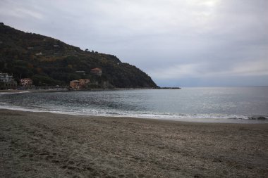 Kışın bulutlu bir günde, kumsalda bir bina, arka planda ağaçlarla kaplı bir uçurum ve uçurumun kenarında bir dalgakıran.
