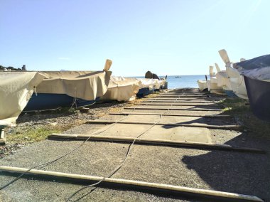 Güneşli bir günde deniz kıyısındaki kayıkhane ve üzeri teknelerle çevrili sahile geçiş.