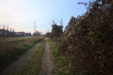 Elektrik direği ve sınırında bir elektrik hattı olan patika, gün batımında İtalya 'nın kırsal kesimindeki bir parkta, bir köyün evleriyle sınırda, ve eğlence kanalının diğer tarafında bir viyadük kanalı ile çevrili.