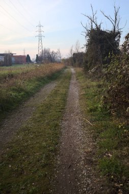 Elektrik direği ve sınırında bir elektrik hattı olan patika, gün batımında İtalya 'nın kırsal kesimindeki bir parkta, bir köyün evleriyle sınırda, ve eğlence kanalının diğer tarafında bir viyadük kanalı ile çevrili.