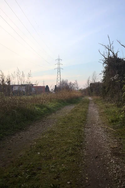 Elektrik direği ve sınırında bir elektrik hattı olan patika, gün batımında İtalya 'nın kırsal kesimindeki bir parkta, bir köyün evleriyle sınırda, ve eğlence kanalının diğer tarafında bir viyadük kanalı ile çevrili.