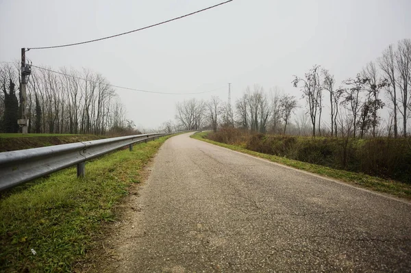 Kışın İtalya kırsalında sisli bir günde, bir su deresi, çıplak ağaçlar ve uzun otlarla çevrili bir viraj yaparak setin üzerindeki yola tırmanmak.