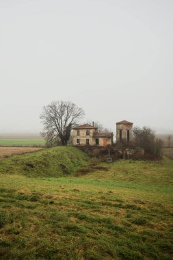 Bir tarlada terk edilmiş bir baraj, yanında çıplak bir ağaç olan bir hendek, İtalya 'nın kışın kırsalında sisli ve bulutlu bir günde.