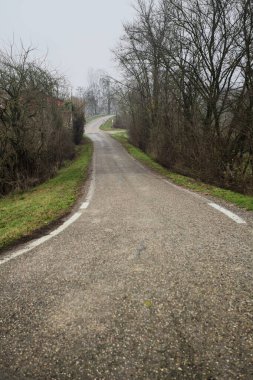 Kışın İtalya kırsalında bulutlu ve sisli bir günde, yol kenarında bir malikanesi olan küçük bir koruluktan geçerek setin tepesine inen bir yol.