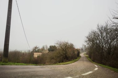 Kışın İtalya kırsalında bulutlu ve sisli bir günde, yol kenarında bir malikanesi olan küçük bir koruluktan geçerek setin tepesine inen bir yol.