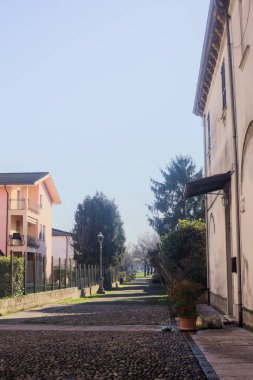 Kışın güneşli bir günde, İtalya kırsalındaki bir köyde, kısmen gölgede, parka giden kaldırımlı bir cadde.