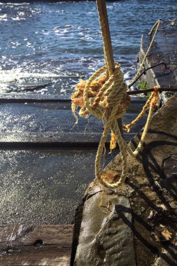 Güneşli bir günde, güneşin betona döküldüğü denizin yanındaki merdivenin kenarındaki direğe bağlanmış sarı halat.