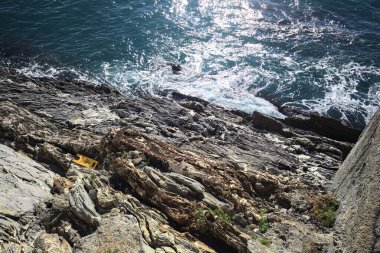 Denizin dalgaları bir uçurumun kayalıklarına çarpıyor. Güneş ışığı yukarıdan görünen suya vuruyor.