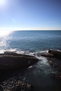 Waves of the sea crushing on the rocks of a cliff with sunlight casted on the water seen from above