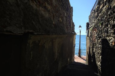 Güneşli bir günde deniz kenarında bir sokak lambasına çıkan taş duvarlar arasındaki dar geçit.